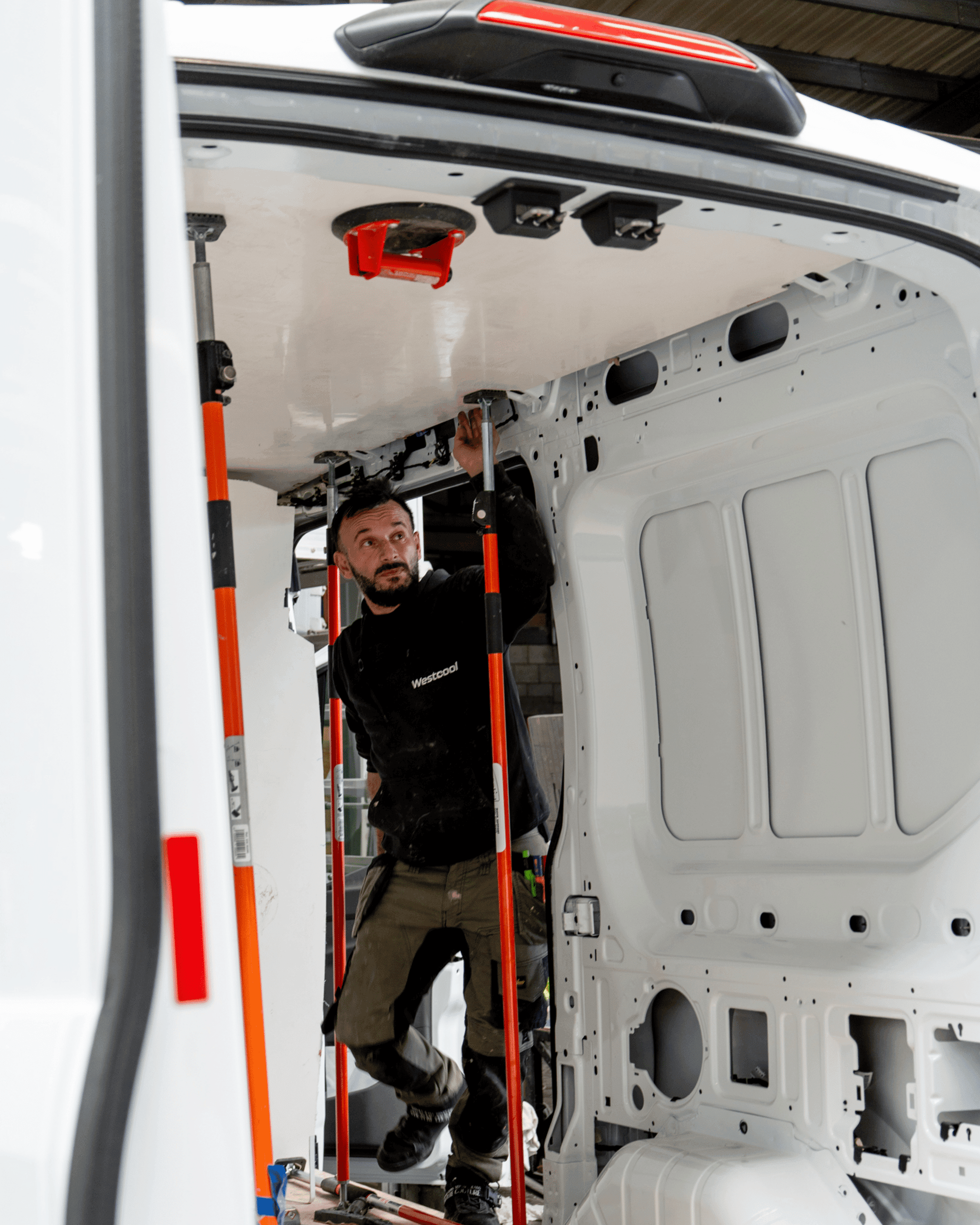 Een technicus klemt met oranje stutten een isolatiepaneel tegen het dak van een witte bestelwagen in opbouw